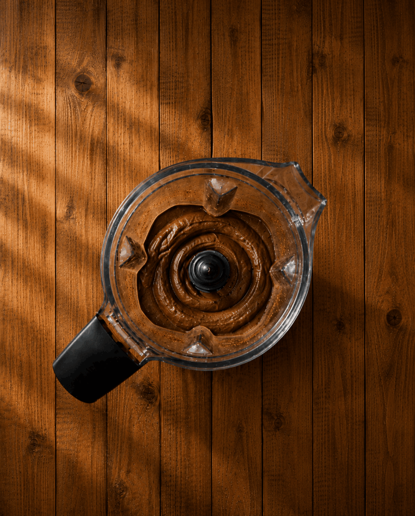 linsen-schoko-waffelteig-cremig-gemixt Draufsicht in einen Mixer mit cremig gemixtem dunklen Linsen-Schokoladen-Waffelteig auf rustikalem Holzuntergrund
