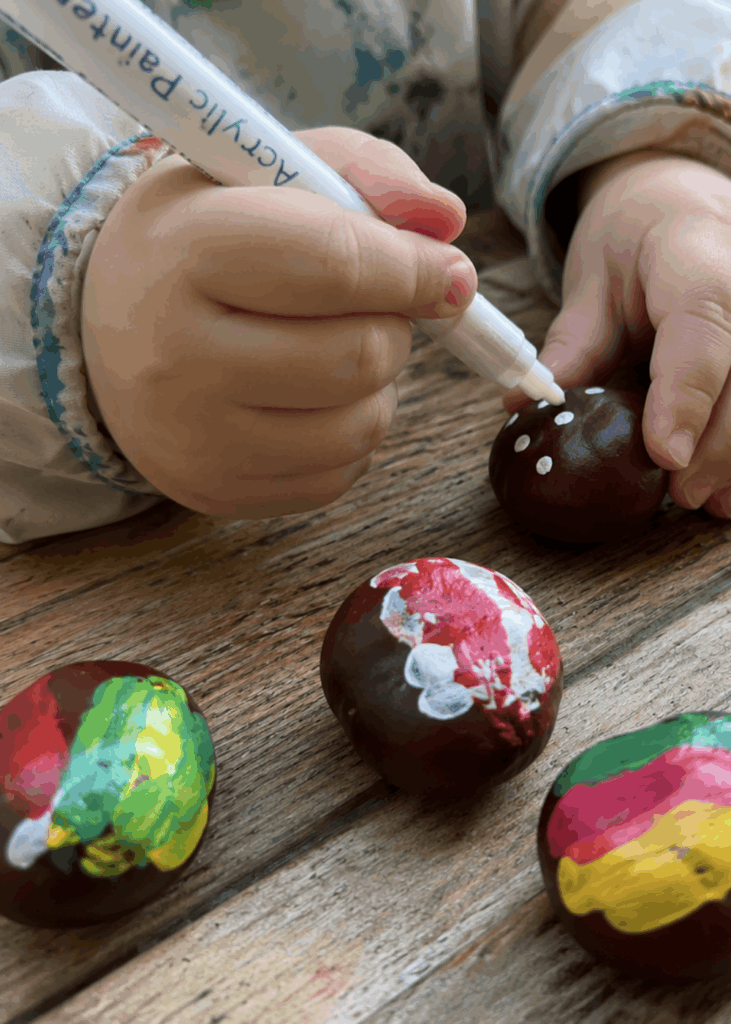 Bunt bemalte Kastanien mit weißen Punktmustern auf Holztisch