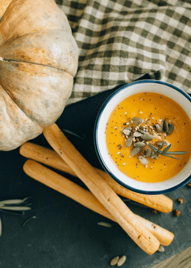 Kürbis-Kokos-Suppe mit Brotstangen und Kernen serviert