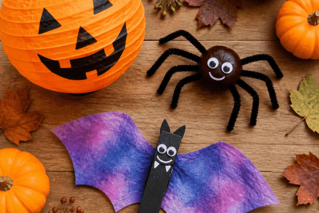 Verschiedene niedliche Halloween-Bastelarbeiten wie Kürbislaterne, Kastanien-Spinne und Kaffeefilter-Fledermaus auf einem Holztisch arrangiert