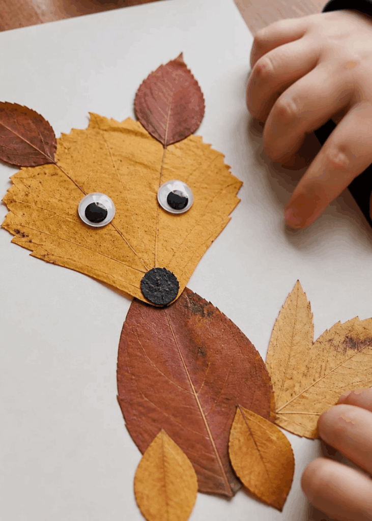 Aus aufgeklebten Herbstblättern gestaltetes Tier mit Wackelaugen auf Papier