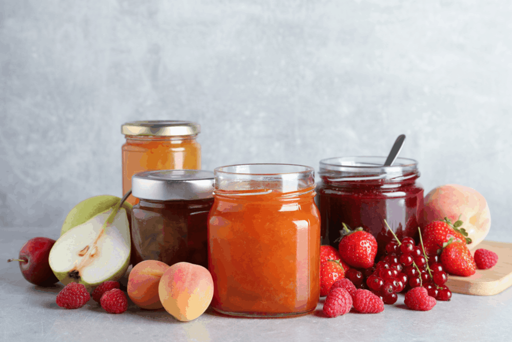 Reihe verschiedener selbstgemachter Marmeladengläser ohne Zucker, umgeben von frischem Obst