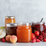 Reihe verschiedener selbstgemachter Marmeladengläser ohne Zucker, umgeben von frischem Obst