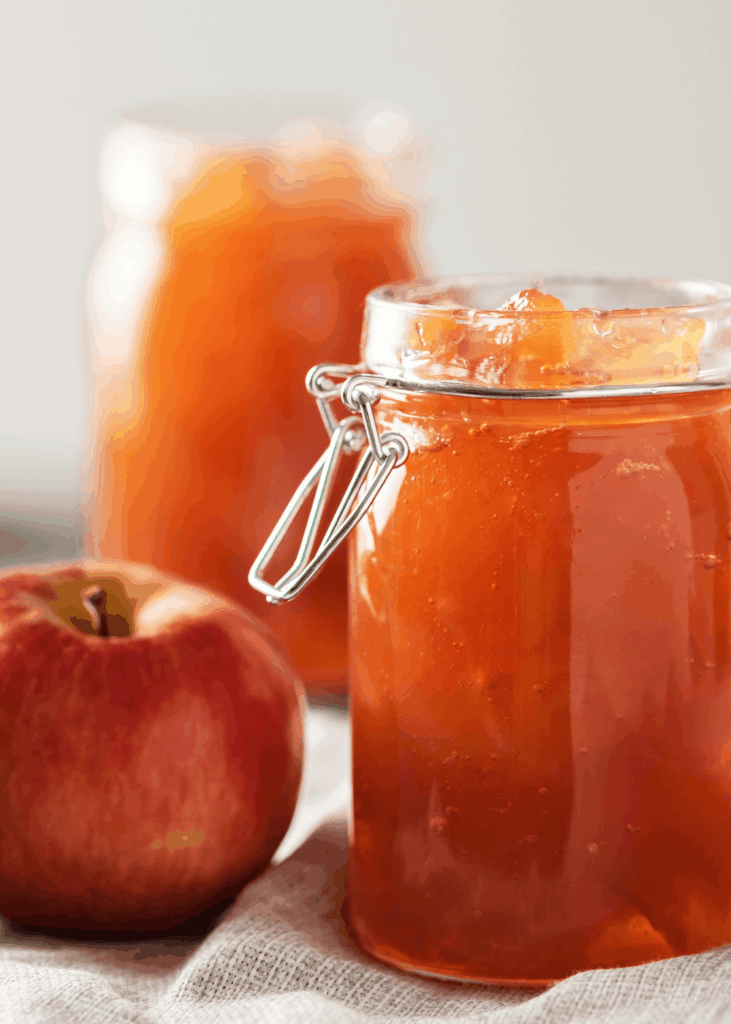 Glas mit klarer Apfelmarmelade und frischem Apfel, ein zweites Glas Marmelade im Hintergrund.