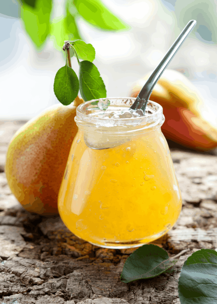Glas mit goldener Birnenmarmelade und Löffel, frische Birne mit Blatt daneben.