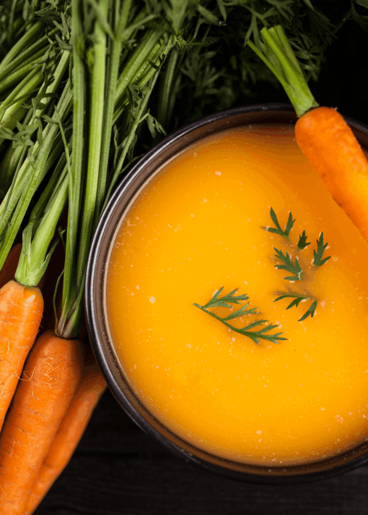 Herbstliche Karottensuppe Orangefarbene Karottensuppe neben frischen Karotten mit grünem Kraut – Karottensuppe Rezept für den Herbst