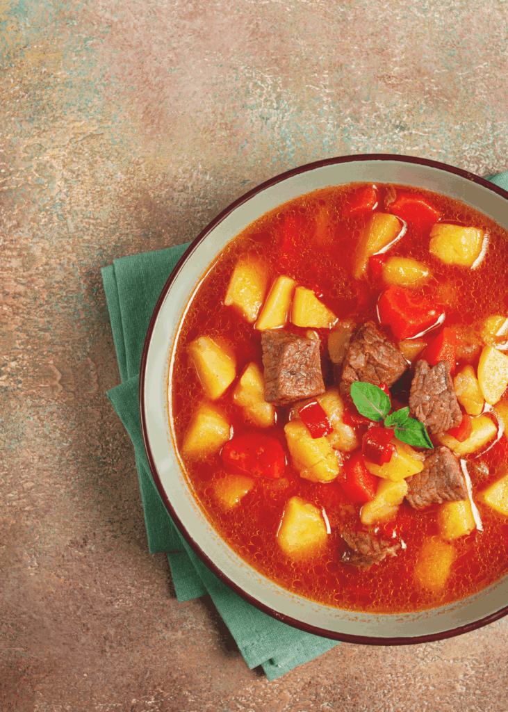 Klassische Gulaschsuppe Rote Gulaschsuppe mit Rindfleisch, Kartoffeln und Paprika auf grünem Tuch – klassisches Gulaschsuppe Rezept